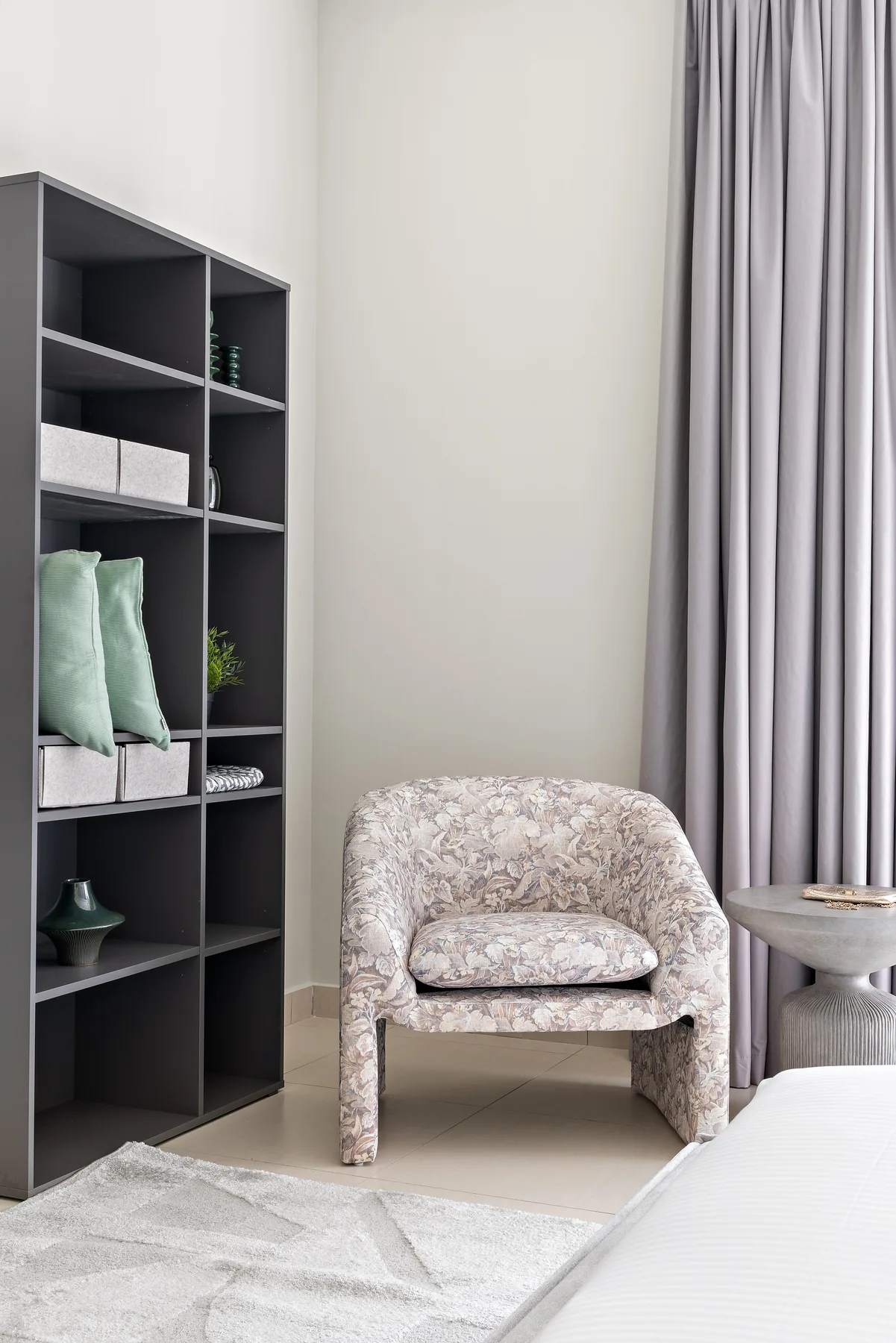 Un sillón estampado está junto a una estantería oscura y cortinas largas.