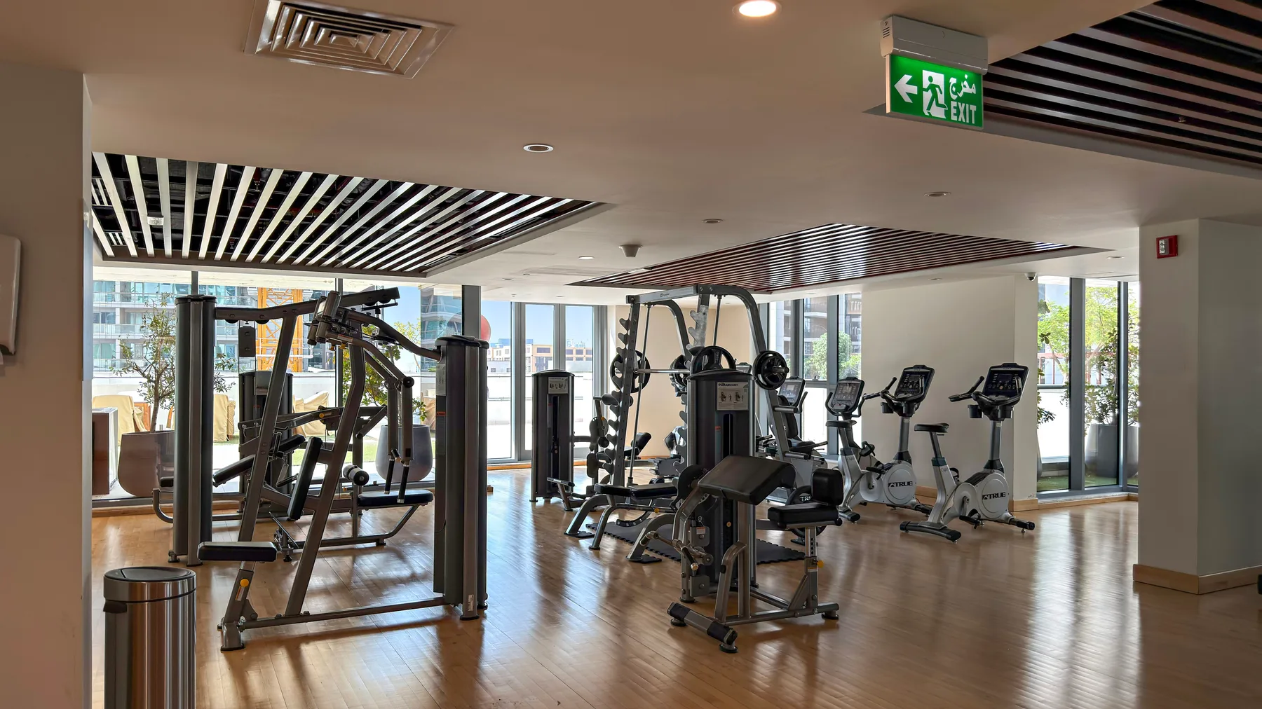 Un gimnasio con máquinas de ejercicio y bicicletas estáticas junto a grandes ventanas.