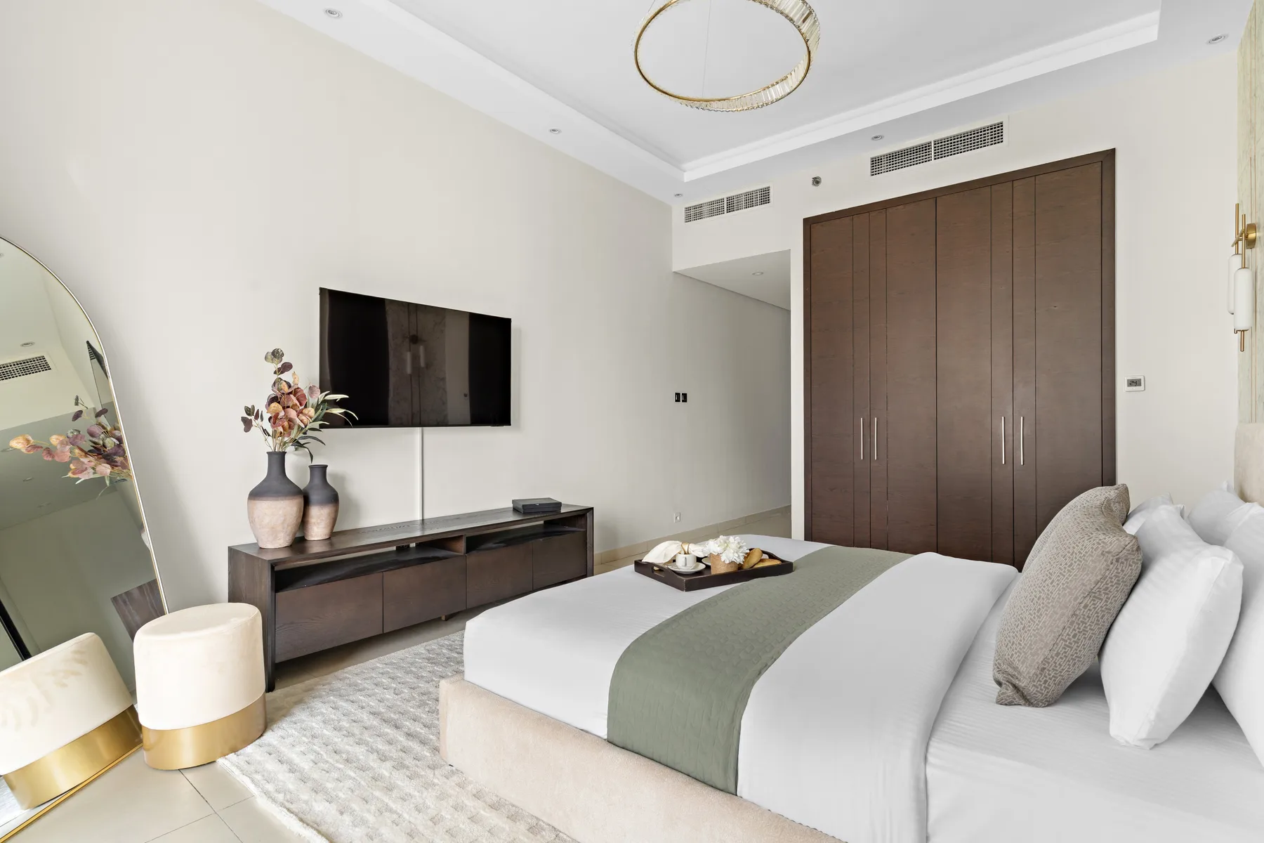 Un dormitorio luminoso con una cama grande, un armario oscuro y un televisor en la pared.