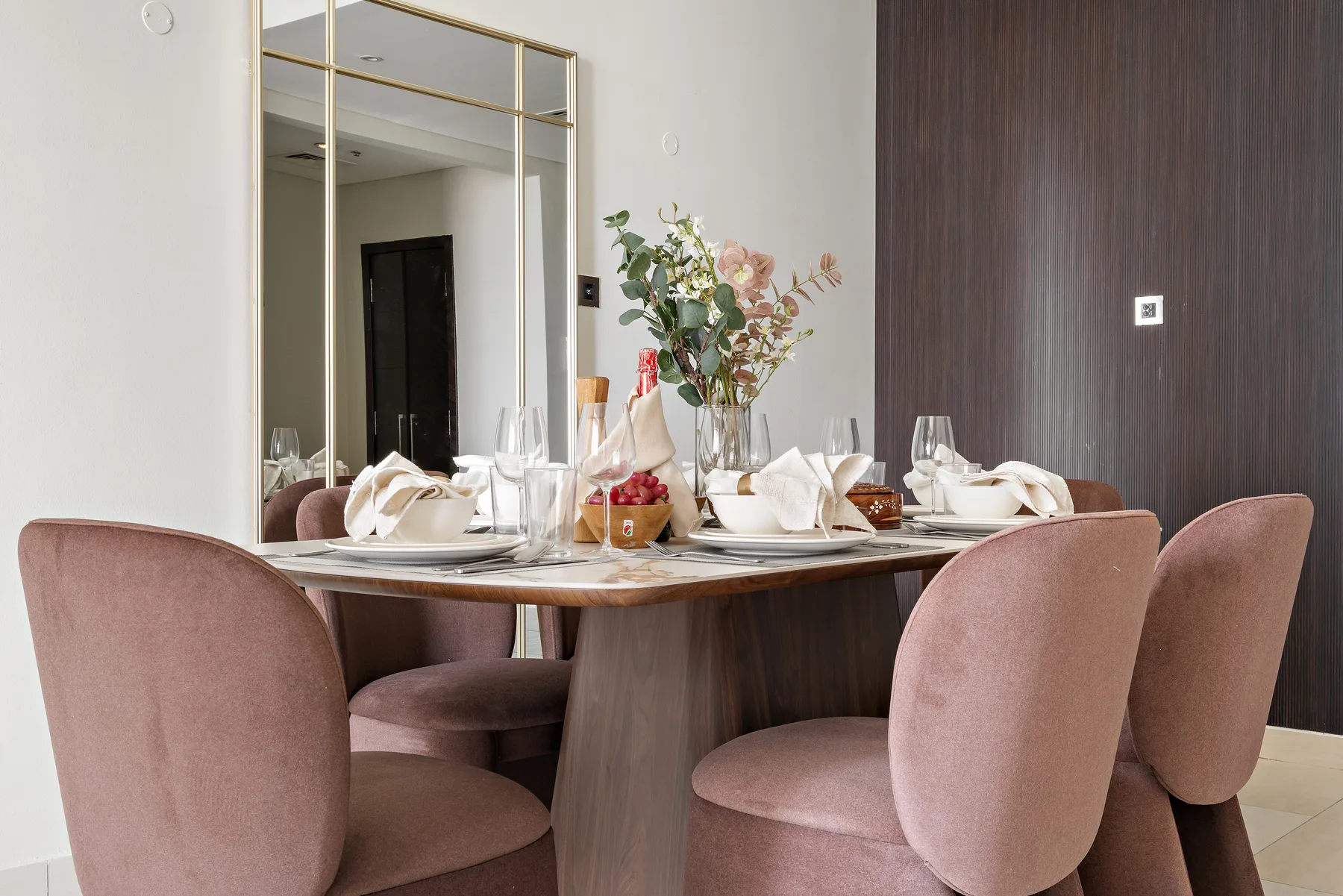 Comedor con una mesa puesta, un arreglo floral y asientos tapizados.