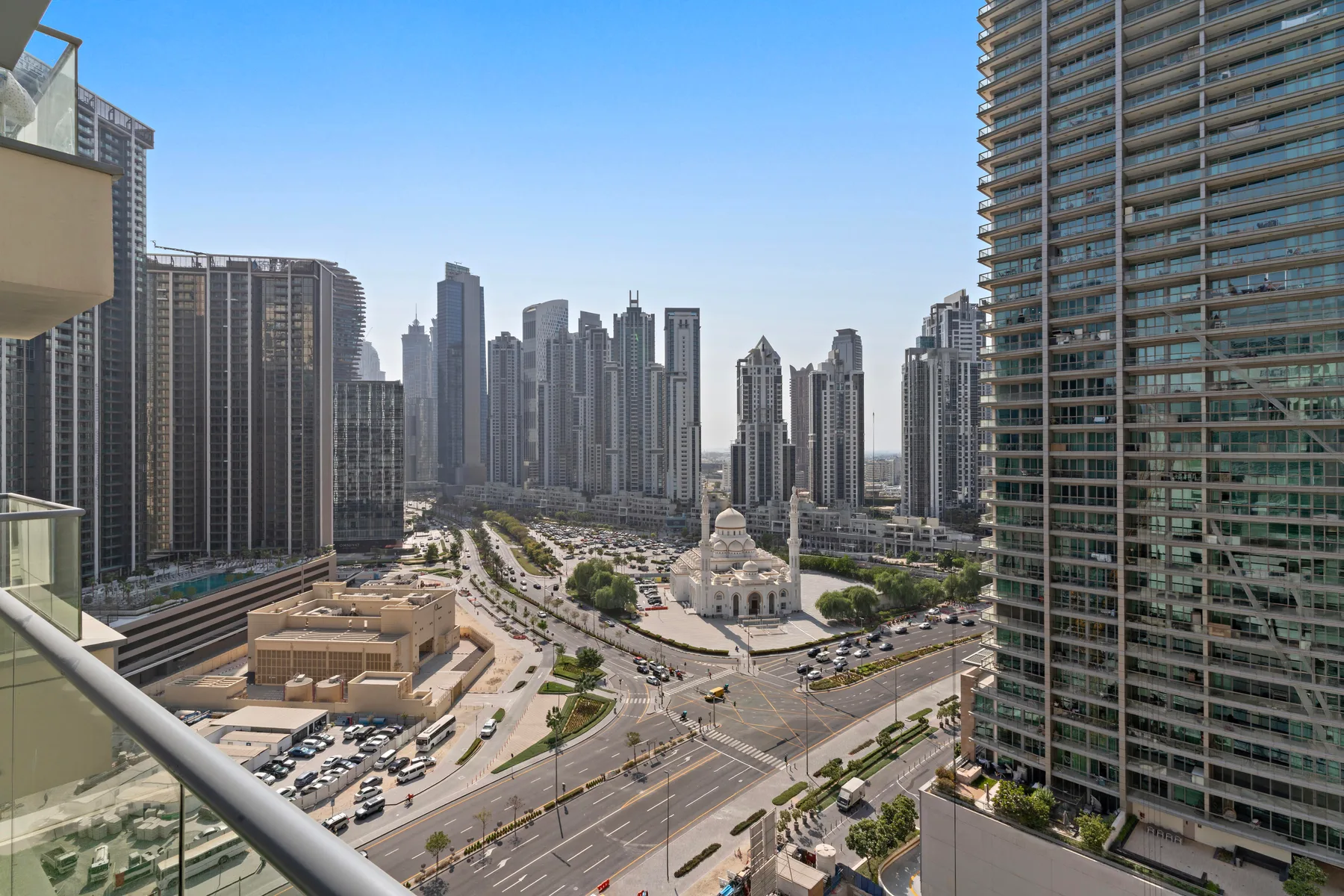 El horizonte urbano se eleva sobre una avenida concurrida, visto desde un balcón.