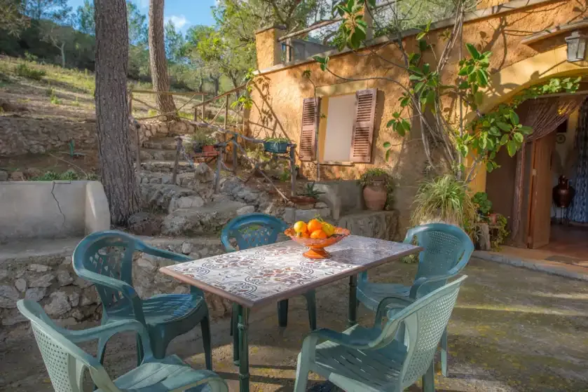 Un patio exterior con una mesa y asientos verdes junto a una casa de piedra.