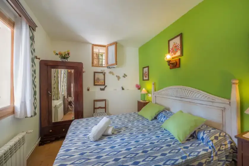 Un dormitorio con una colcha estampada, una pared verde y una ventana.