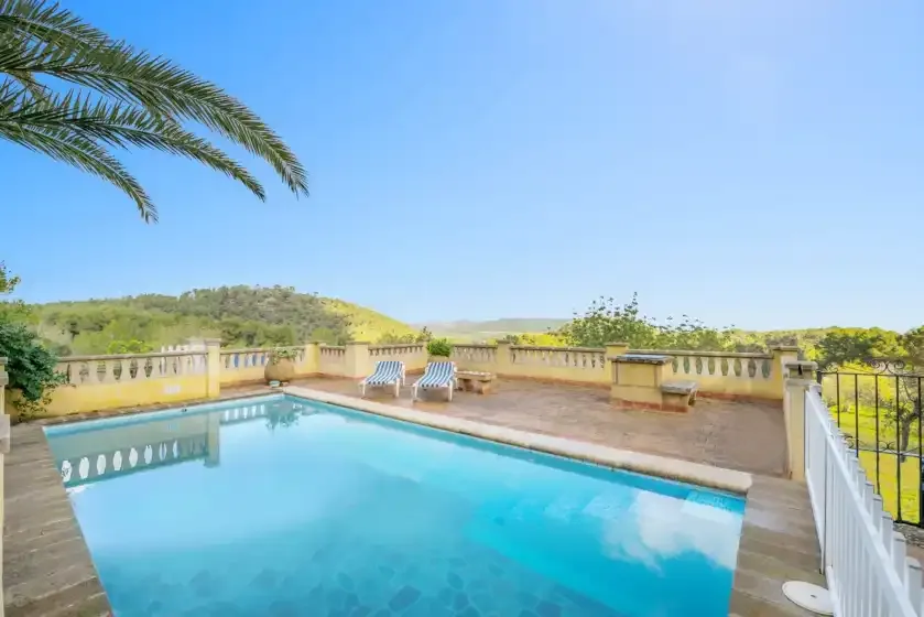 A terrace with a swimming pool, lounge seating, and views of the surrounding hills.