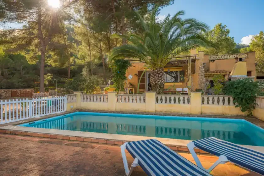 An outdoor swimming pool sits beside a garden and a tan building.
