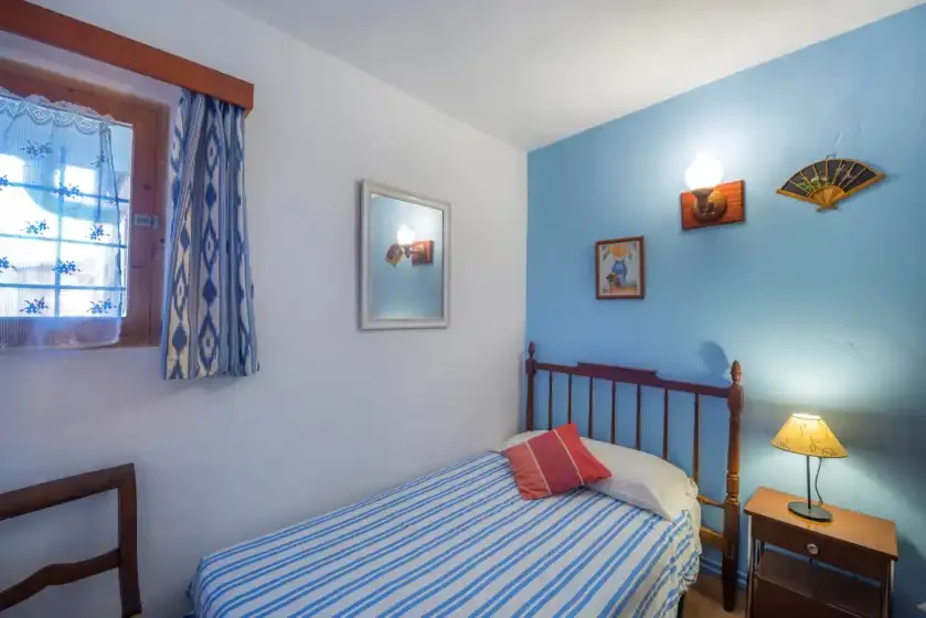 Un dormitorio con una cama individual, ropa de cama a rayas y una ventana con cortinas.