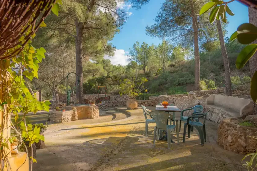 Un patio exterior con una mesa y asientos junto a un muro bajo de piedra.