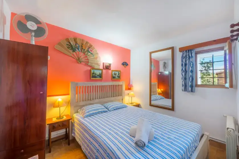Un dormitorio con una colcha a rayas, mesitas de noche y una ventana.
