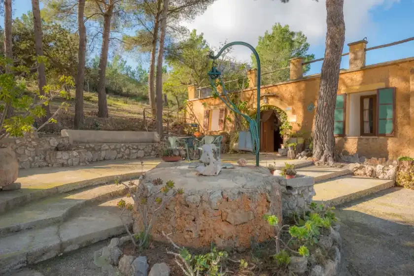 Un patio de piedra con un pozo central frente a un edificio rústico.
