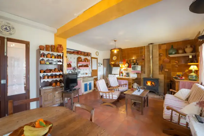 Una sala de estar rústica con asientos, estanterías de madera y una chimenea encendida.