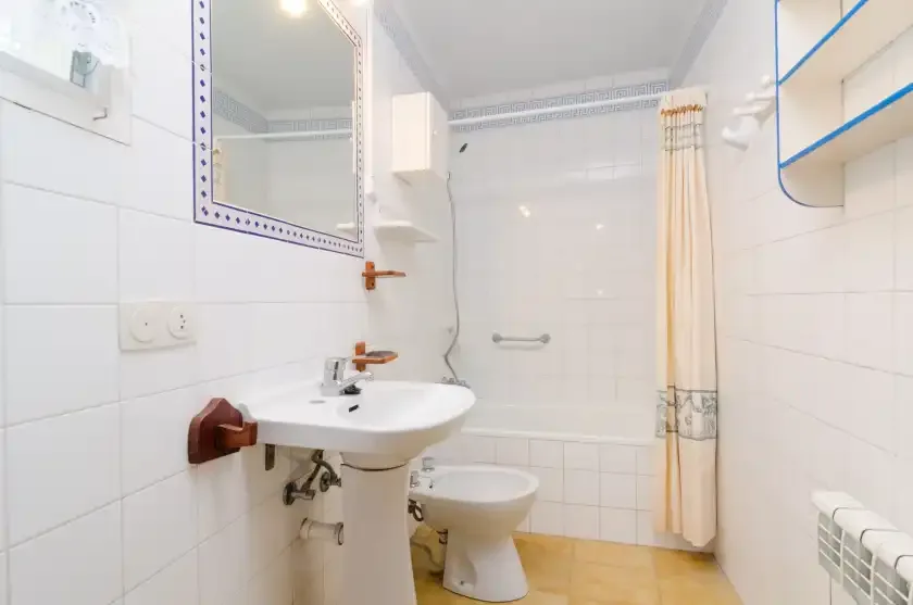 Un baño alicatado con lavabo, inodoro y cortina de ducha.