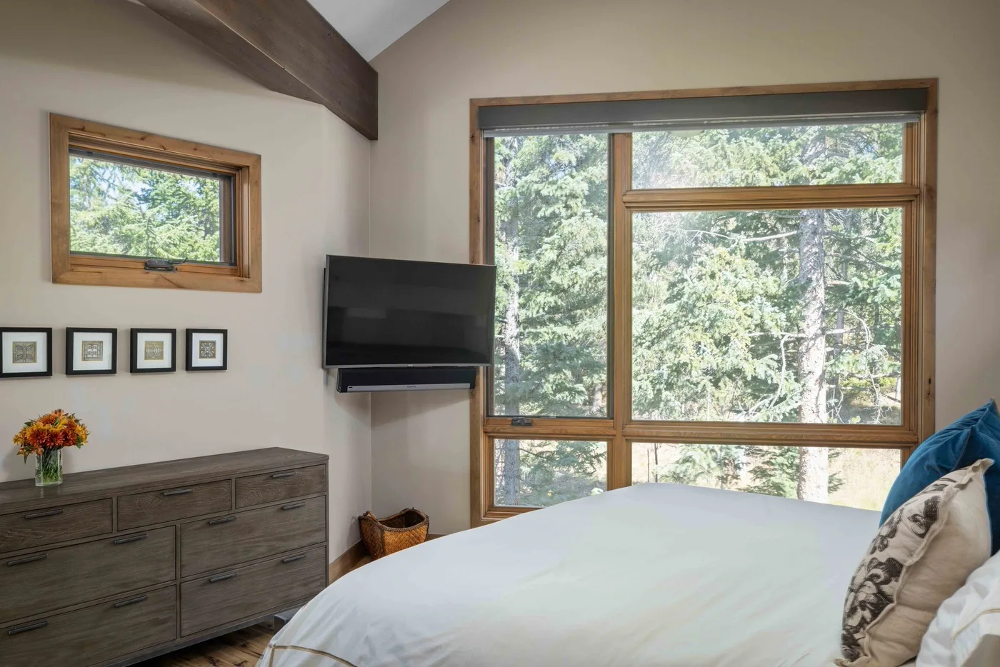 A bedroom with a bed, dresser, and large windows overlooking trees.