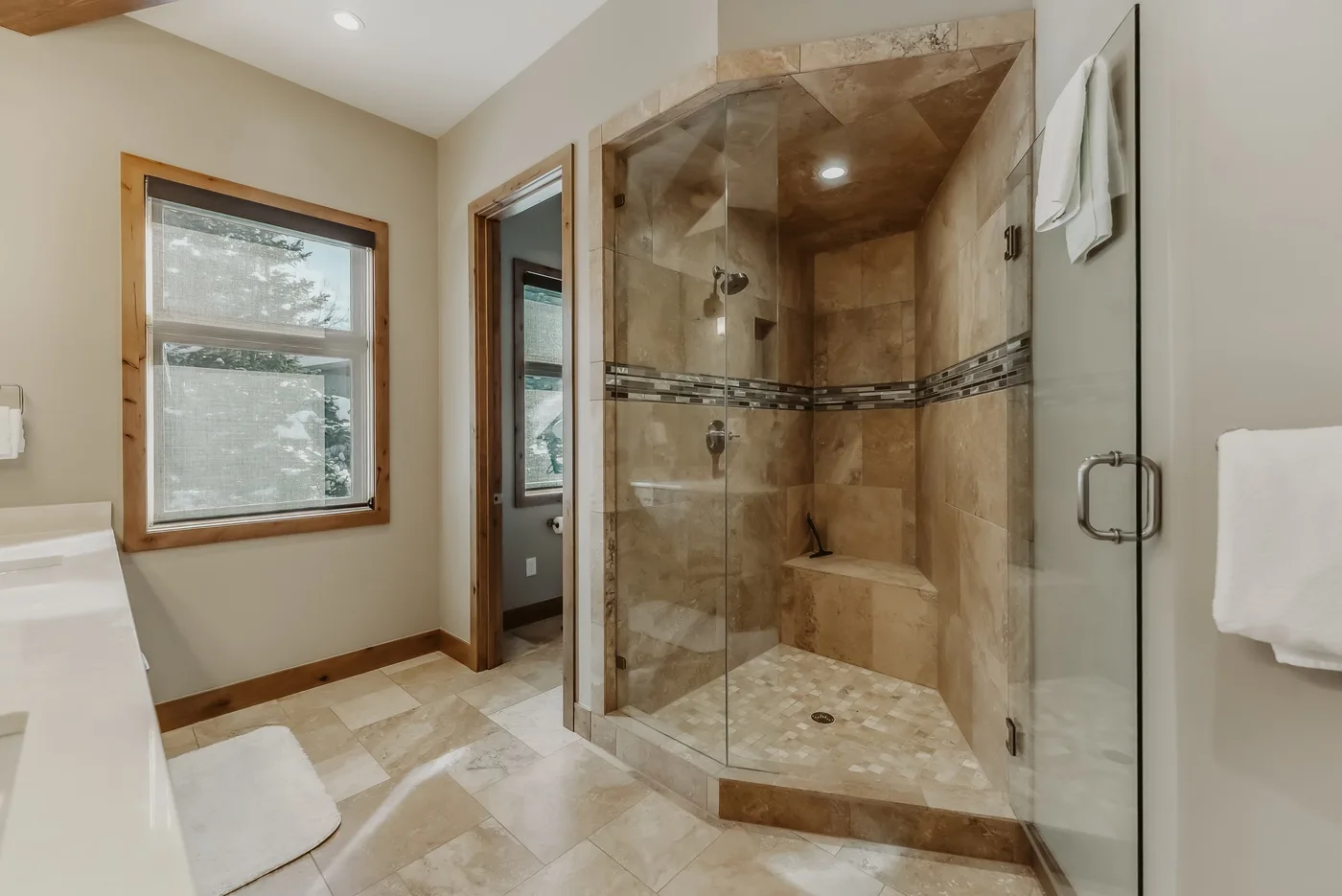 A bathroom with a glass-enclosed shower and a window.