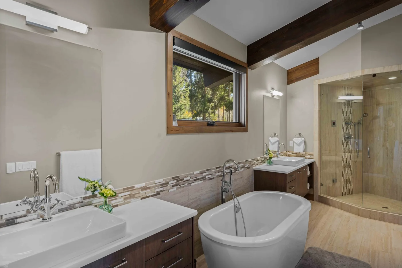 A bathroom with a bathtub, double sink, and glass shower area.