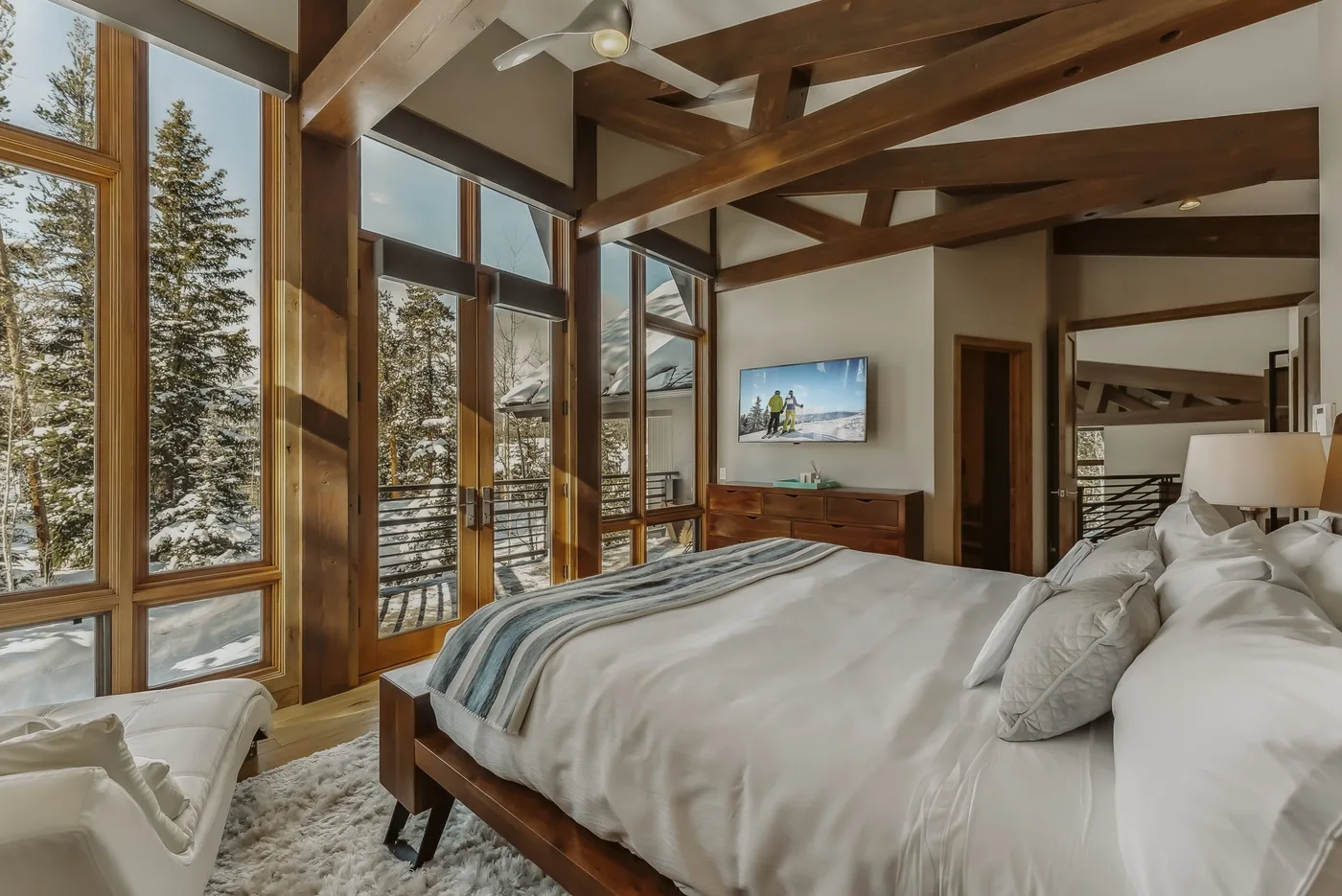 A bedroom with a large bed, tall windows, and exposed wooden beams.