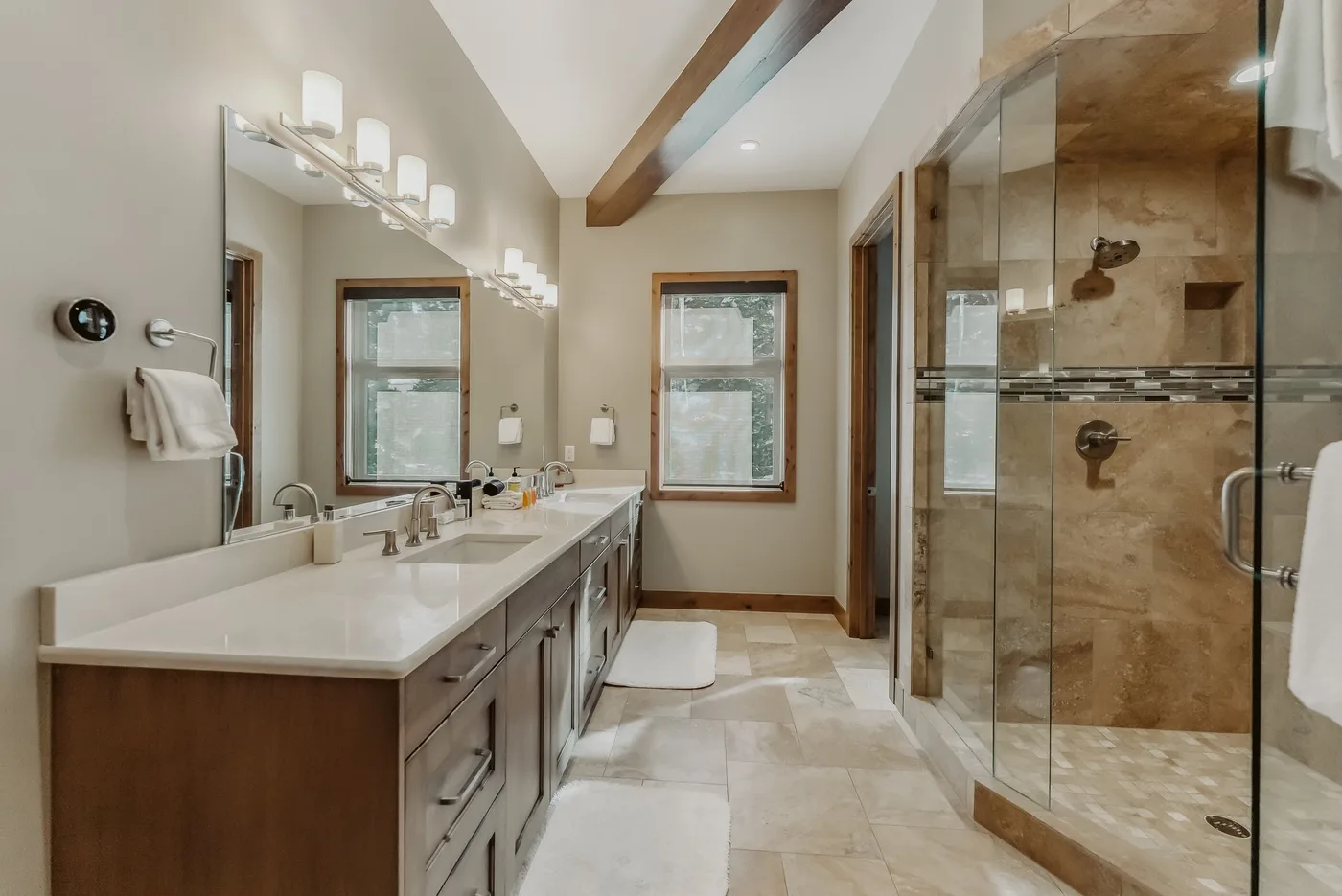 A bright bathroom with a long vanity, windows, and a glass shower.