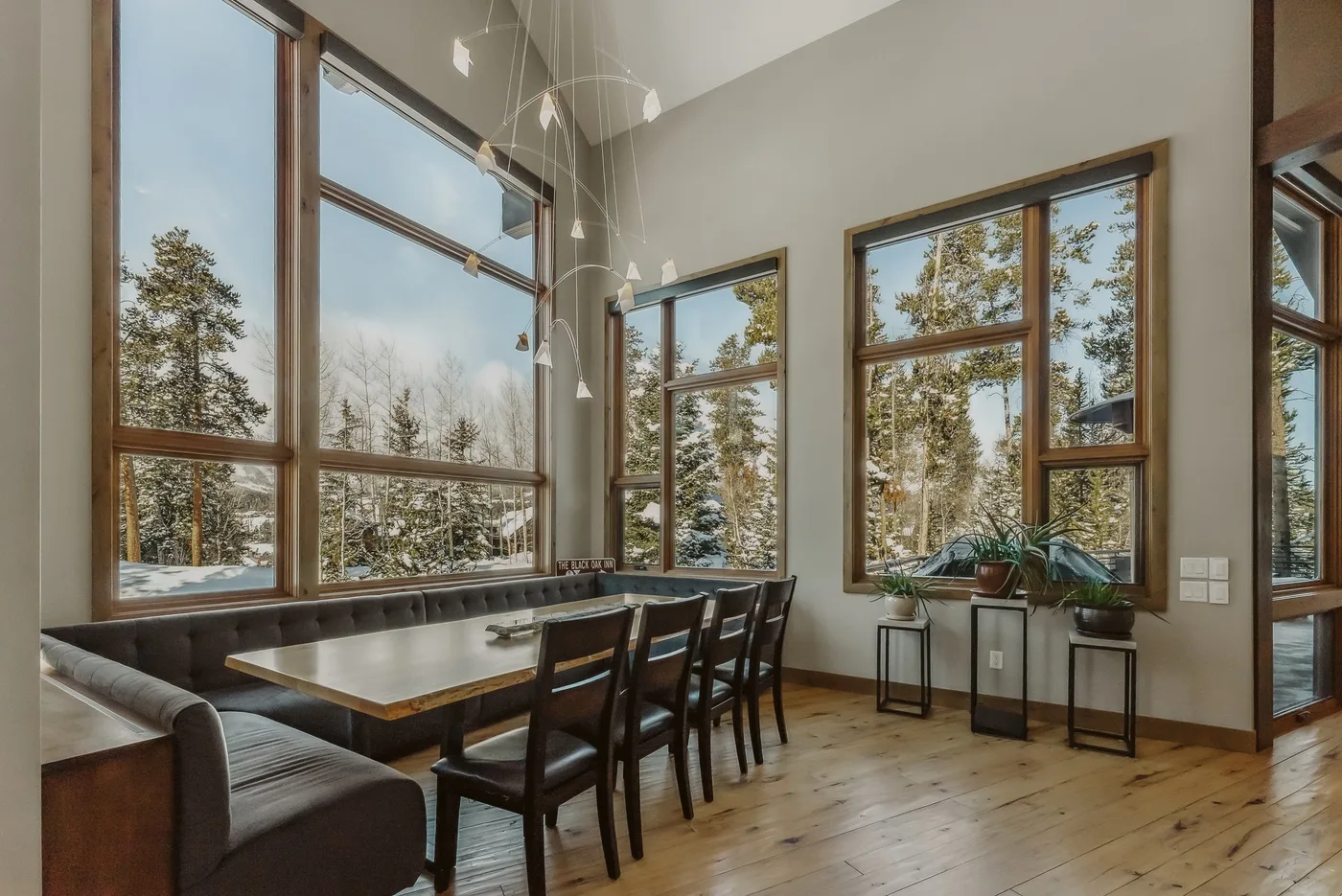 A dining area with a long table and large windows overlooking trees.