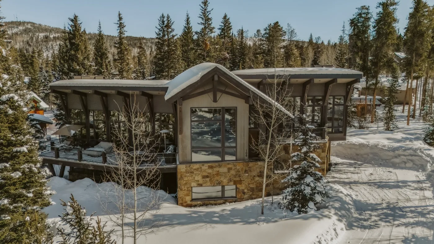 A modern building sits amid snow-covered ground and evergreen trees.