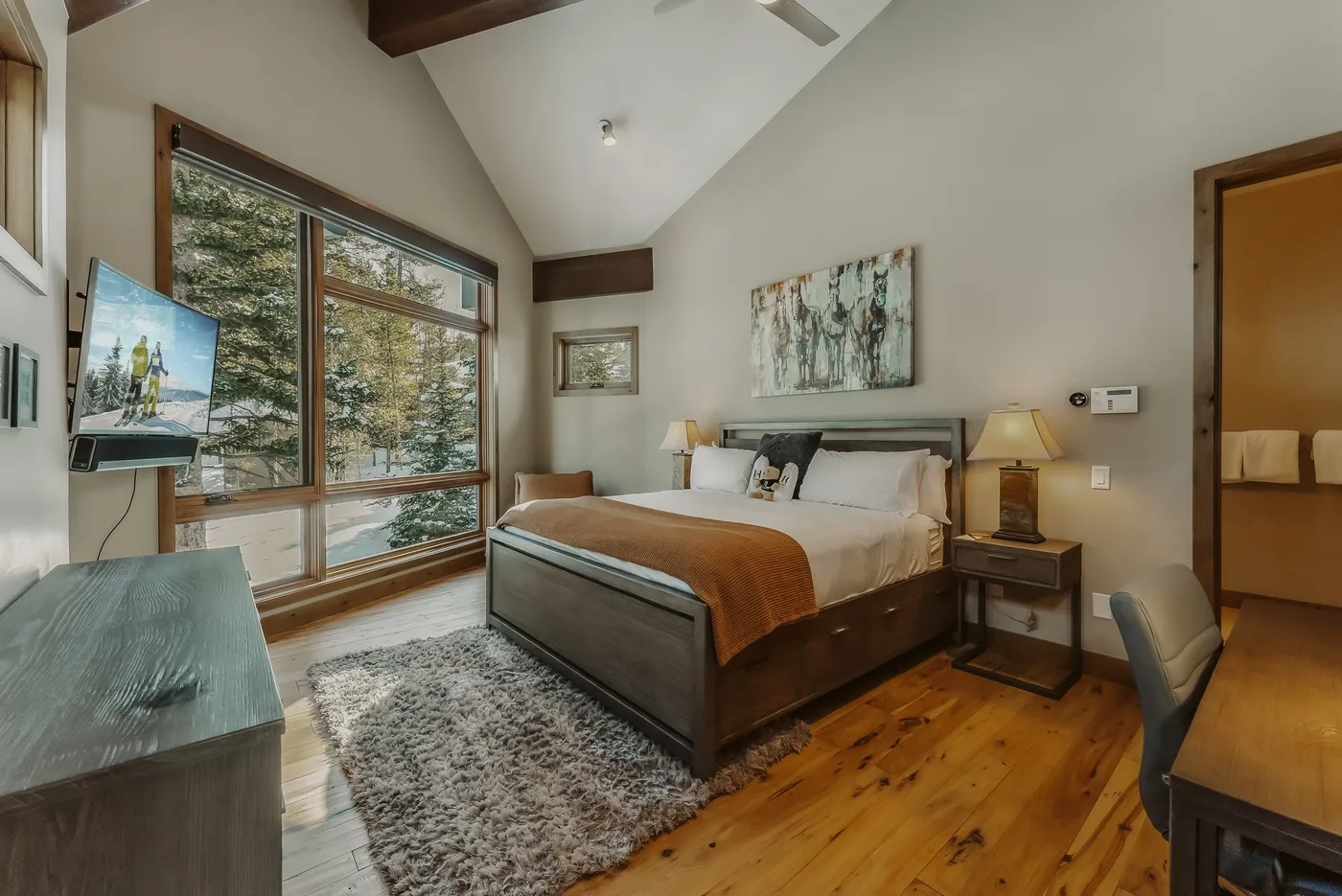 A bedroom with a bed, large windows, and a sloped ceiling.
