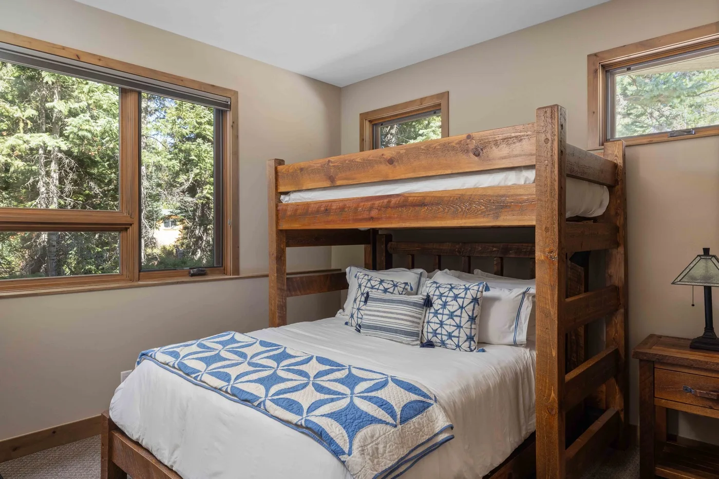 A bedroom with a wooden bunk bed and large windows overlooking trees.