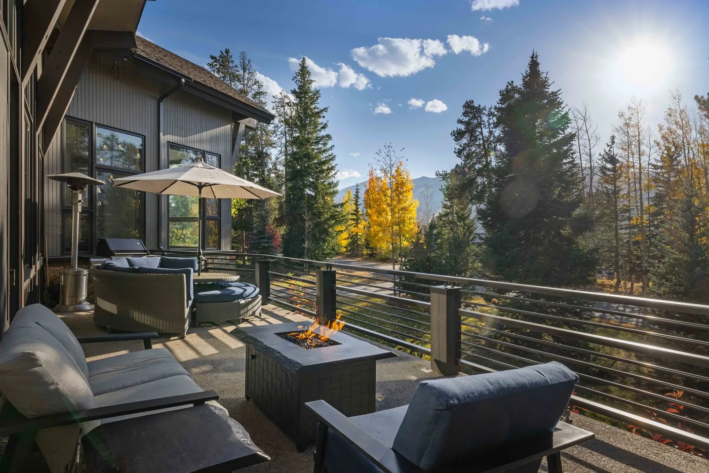 An outdoor deck with seating and a fire table overlooks a tree-lined landscape.