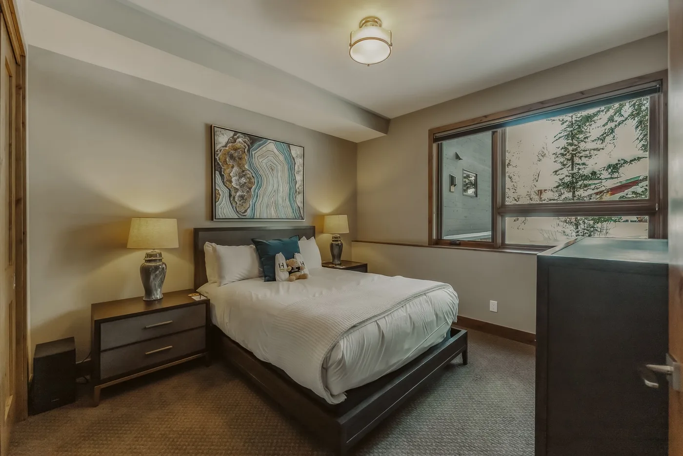 A bedroom with a bed, bedside tables, and a large window.
