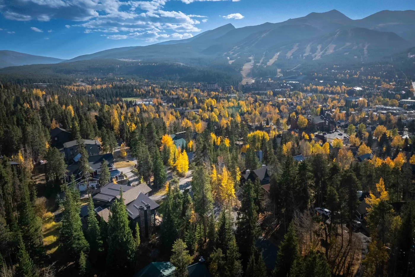 A mountain town sits among colorful autumn trees beneath a broad mountain range.