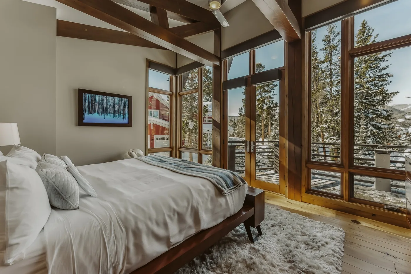 A bedroom with a neatly made bed and large windows overlooking trees.