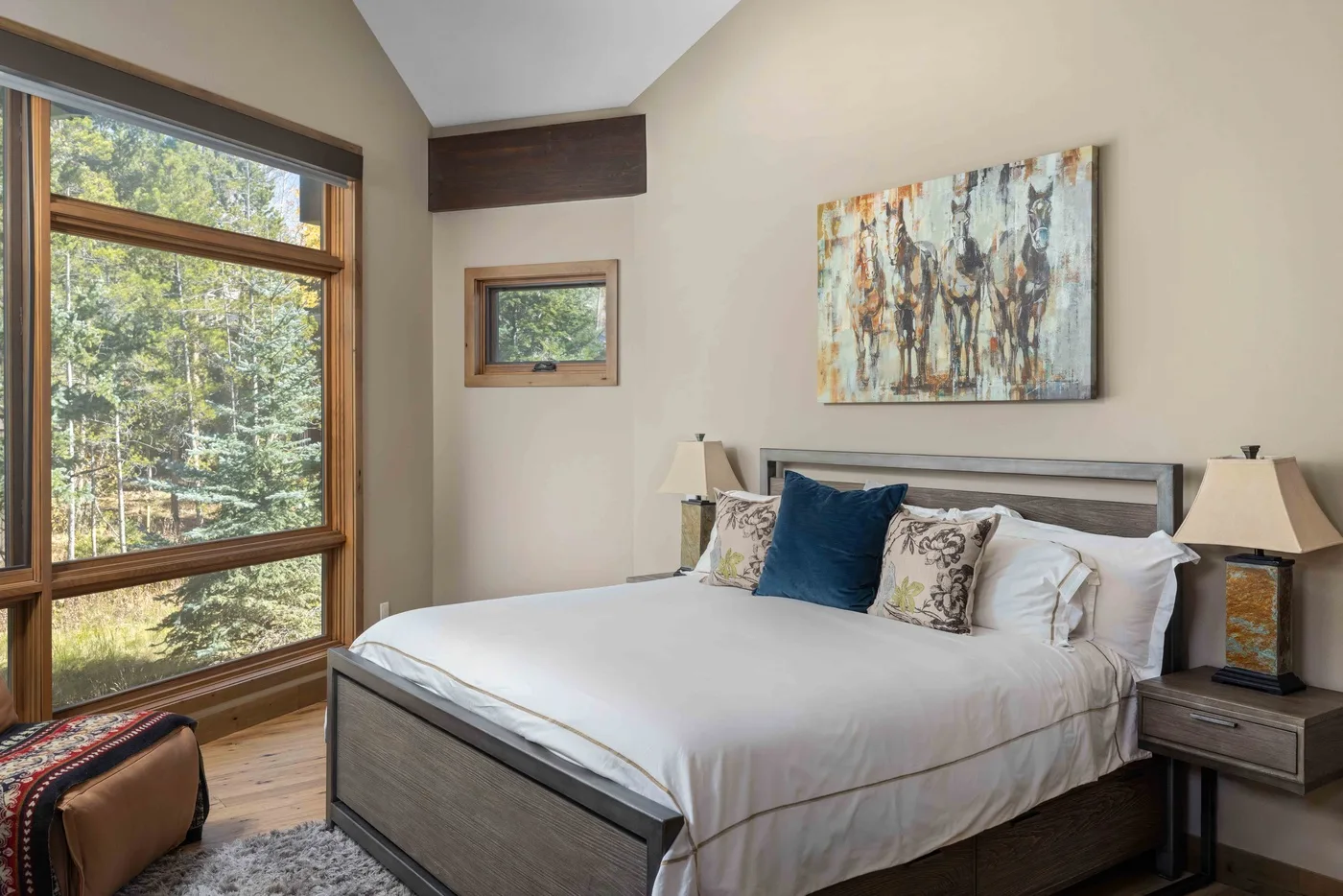 A bedroom with a neatly made bed and large windows overlooking trees.