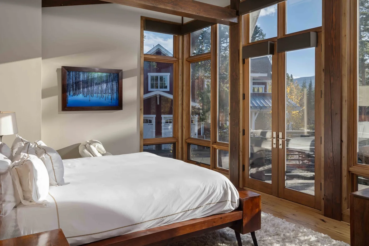 A bright bedroom with a bed beside tall windows and glass doors.