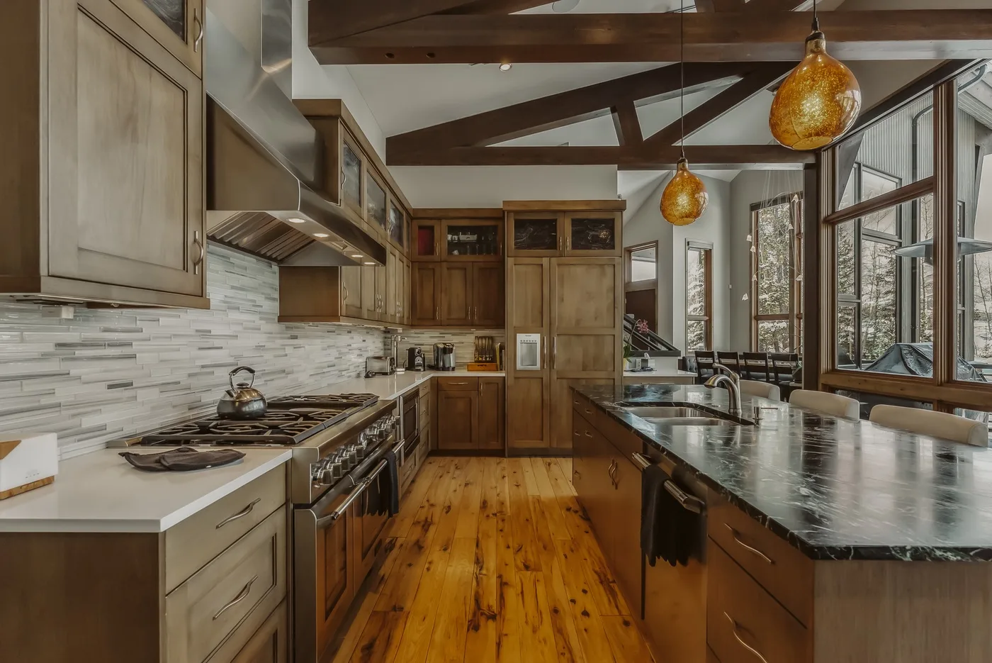 A spacious kitchen with wood cabinetry, stone counters, and large windows.
