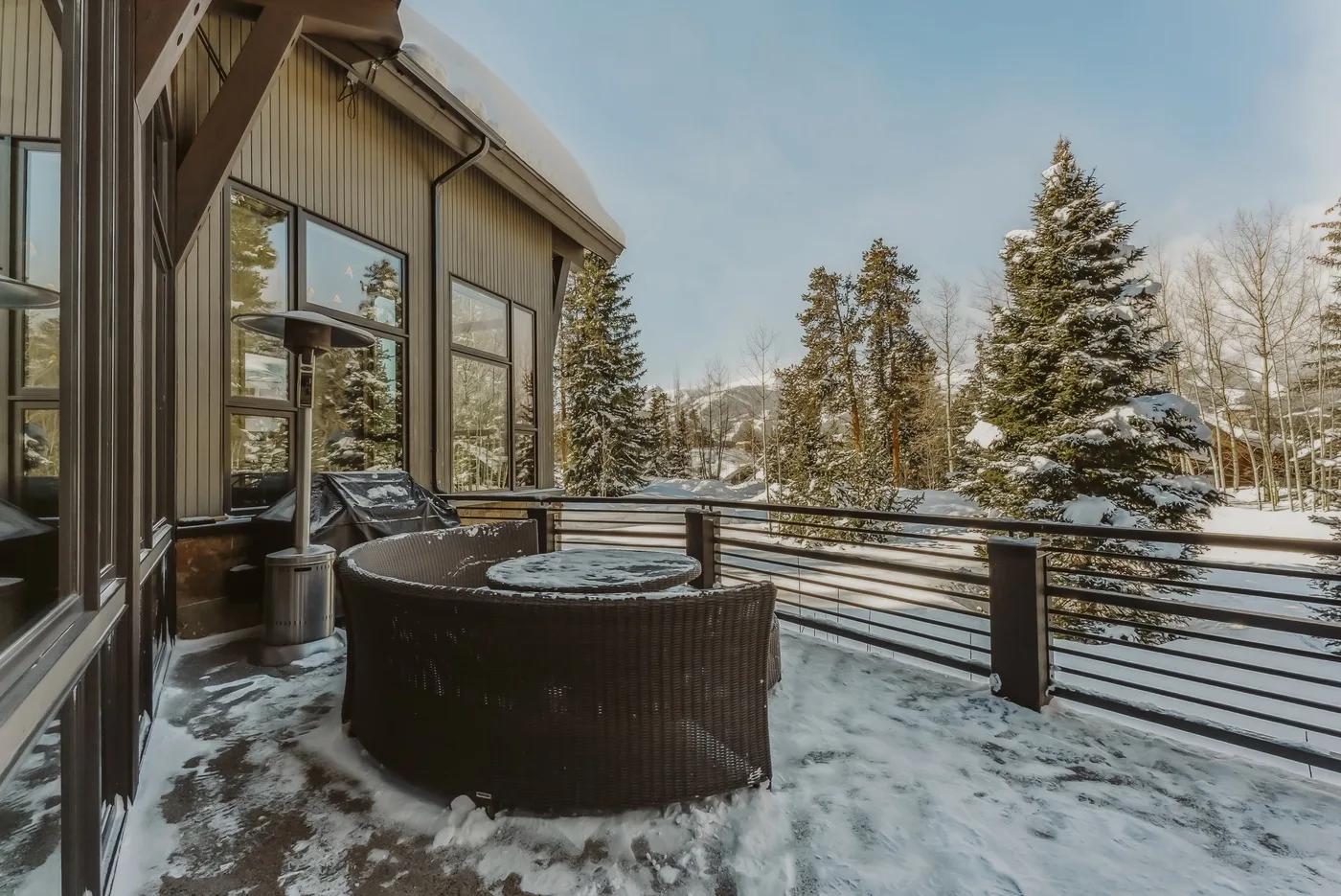 A snow-covered outdoor patio beside a modern building overlooks a wooded landscape.