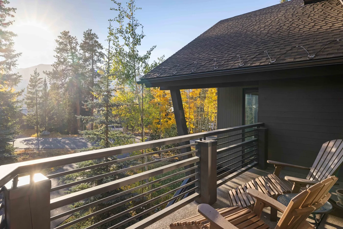 A wooden deck beside a dark building overlooks a sunlit, wooded landscape.
