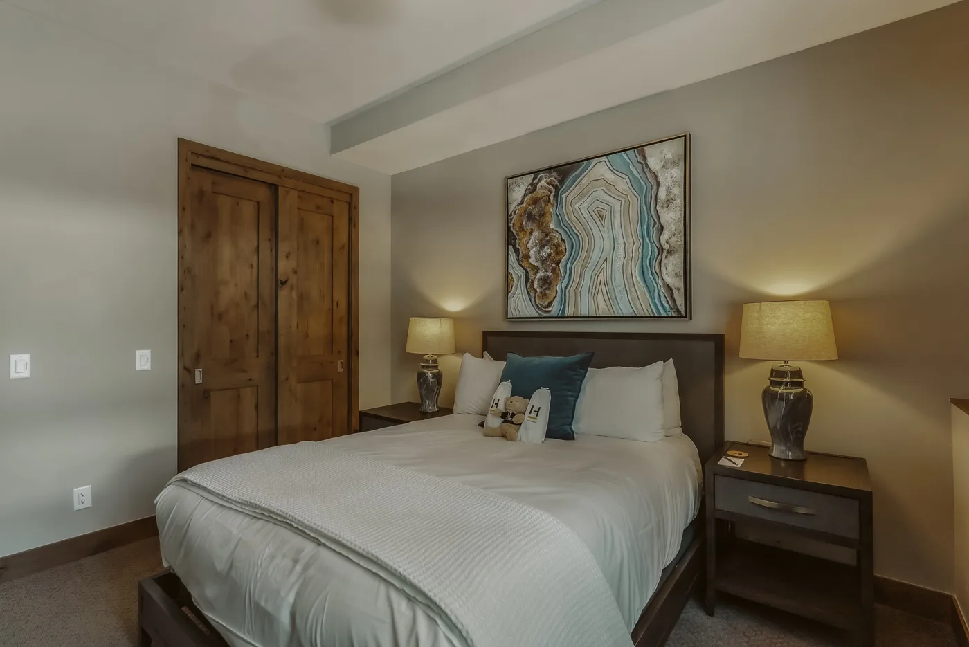 A bedroom with a large bed, wooden wardrobe, and framed artwork above the headboard.