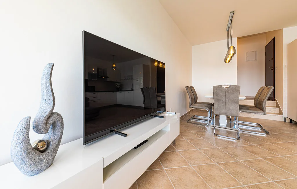 Un comedor con mesa y sillas está junto a un televisor sobre un mueble blanco.