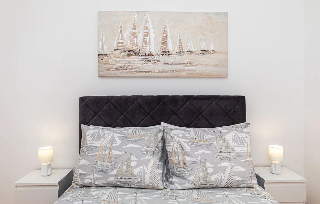 Un dormitorio con una cama tapizada oscura y ropa de cama con motivos de veleros.