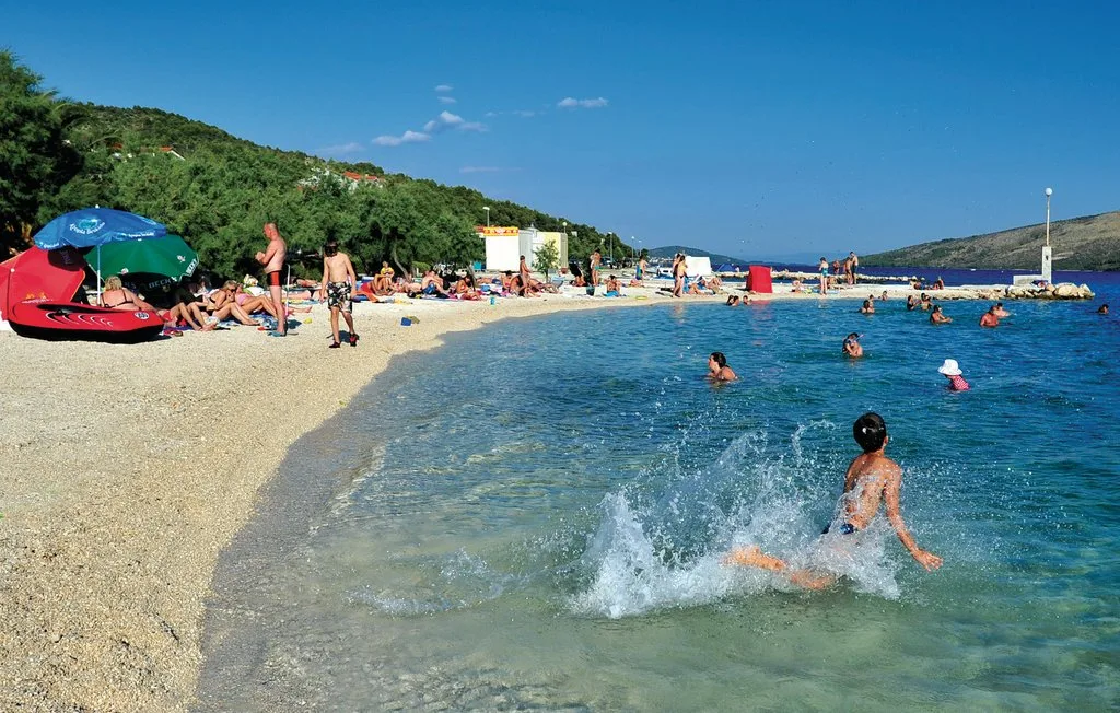 Una playa concurrida bordea aguas claras, con bañistas y personas tomando el sol.