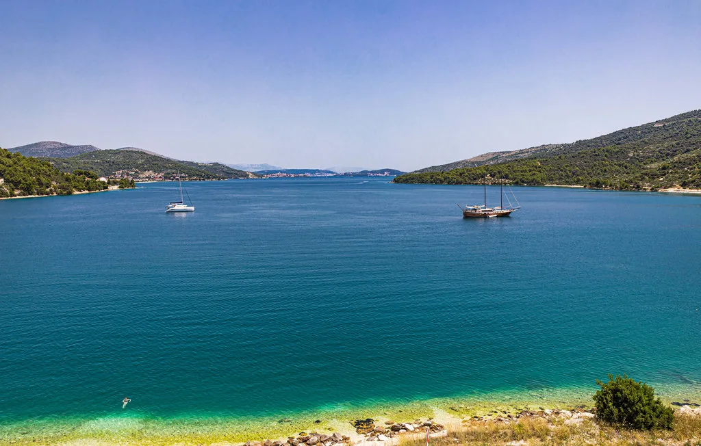 Una bahía costera con aguas turquesas, barcos anclados y colinas verdes junto a la costa.