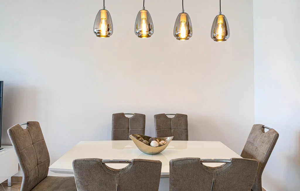Comedor con una mesa rectangular, asientos tapizados y lámparas colgantes.