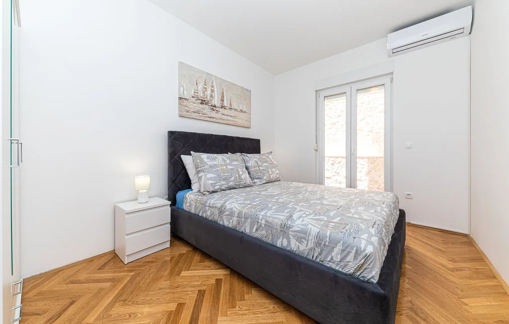 Un dormitorio con cama doble, mesita de noche y suelo de madera en espiga.