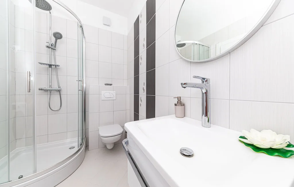 Un baño luminoso con azulejos, una ducha de vidrio y un lavabo blanco.