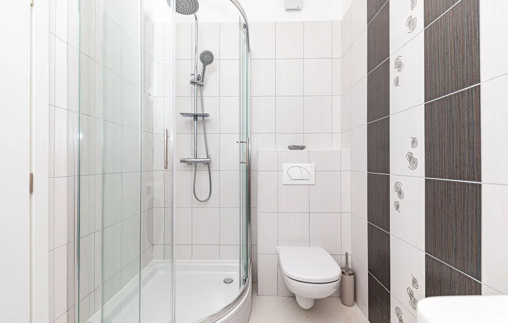 Un baño alicatado con ducha de vidrio e inodoro suspendido.