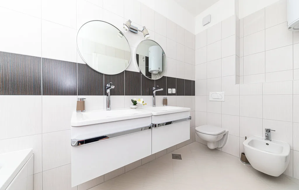 Un baño alicatado con lavabo doble y accesorios montados en la pared.