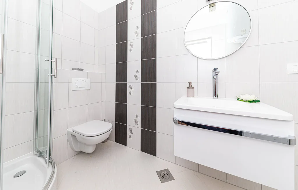 Un baño moderno con ducha de vidrio, inodoro suspendido y lavabo flotante.