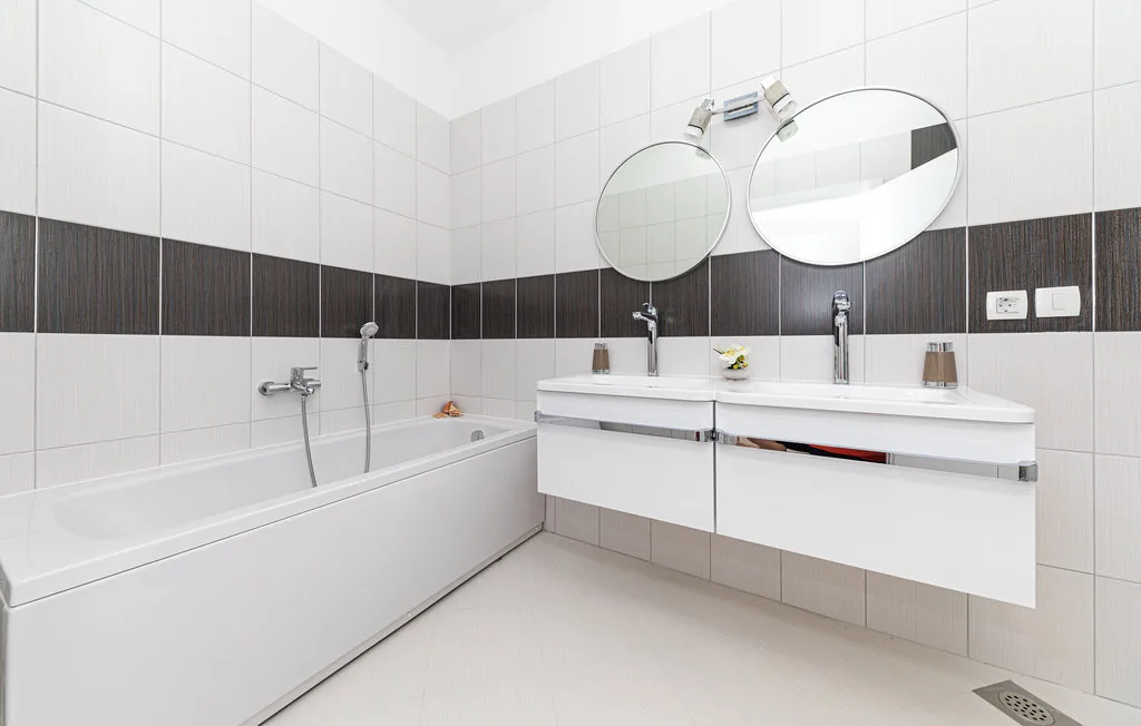 Un baño alicatado con bañera y lavabo doble.