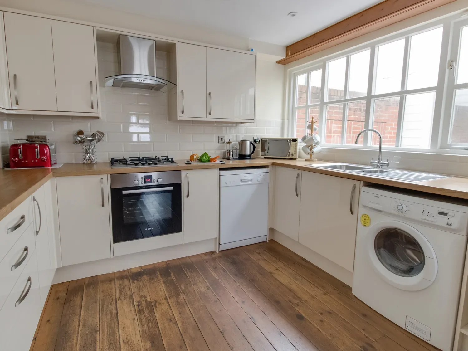 A kitchen with white cabinets wooden countertops and appliances including oven dishwasher and washing machine at Georges House in Brewers Quay Harbour