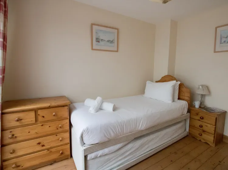 A bedroom with a neatly made bed, wooden dressers, and framed pictures.