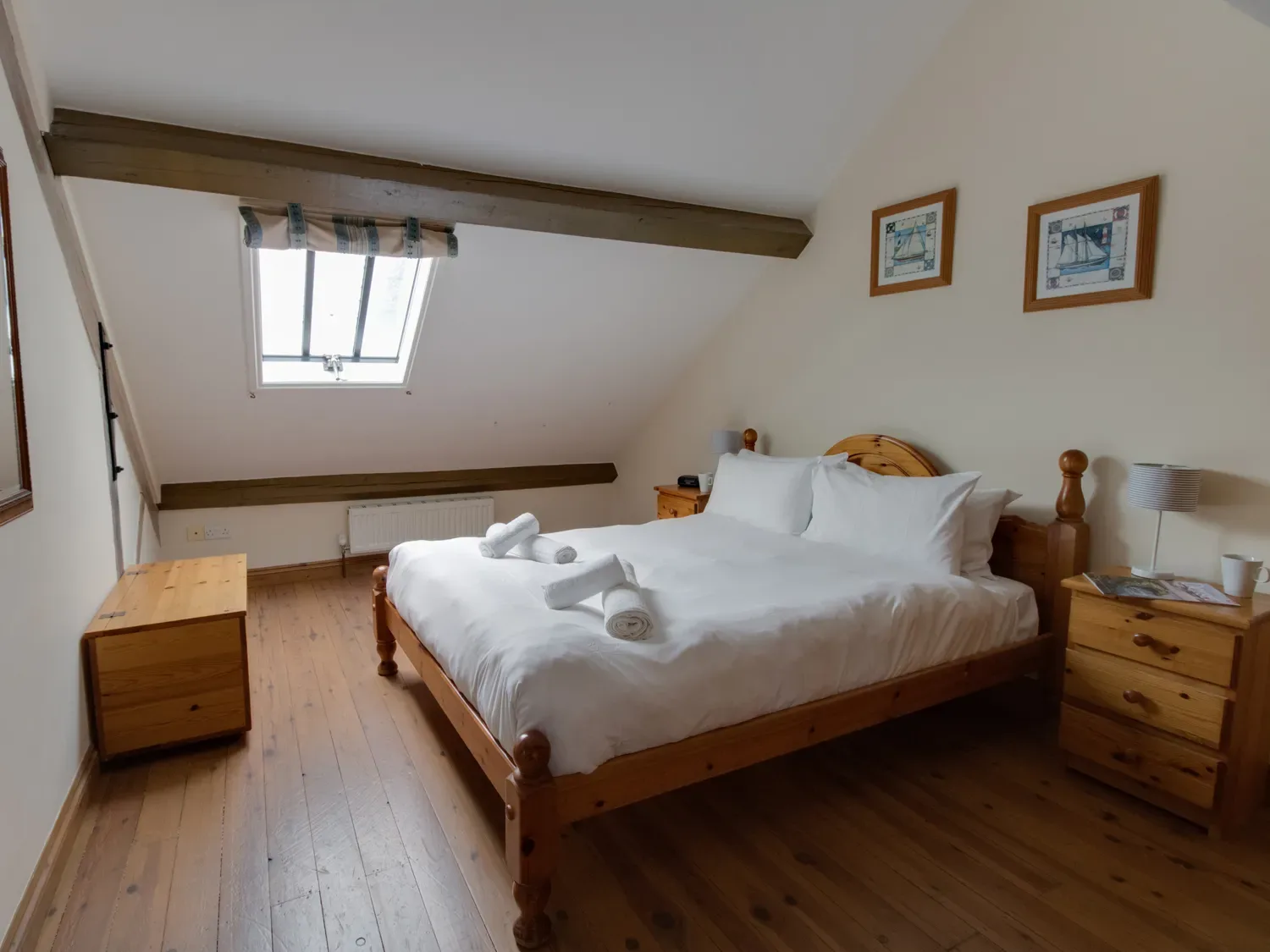 A bedroom with a wooden bed, white bedding, and a skylight.