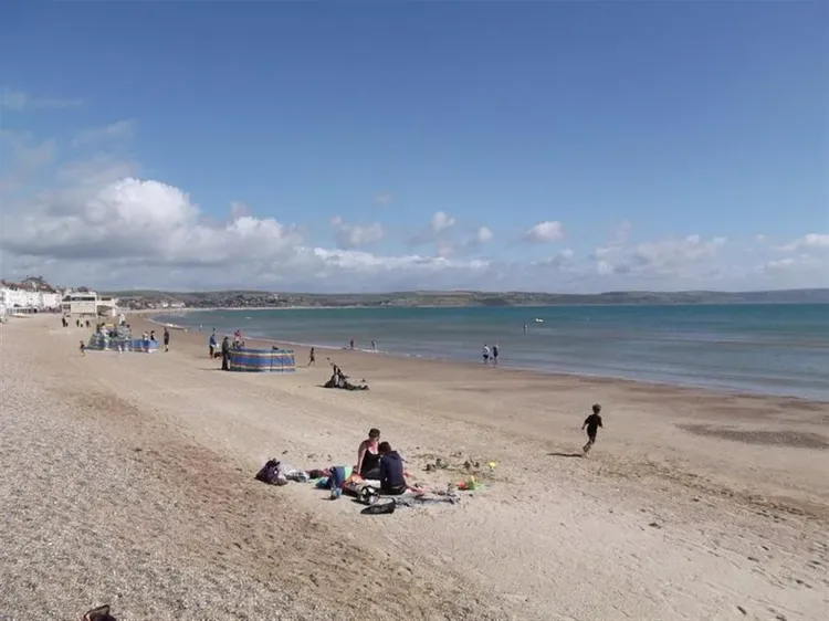 A sandy beach stretches beside calm water, with people relaxing along the shore.