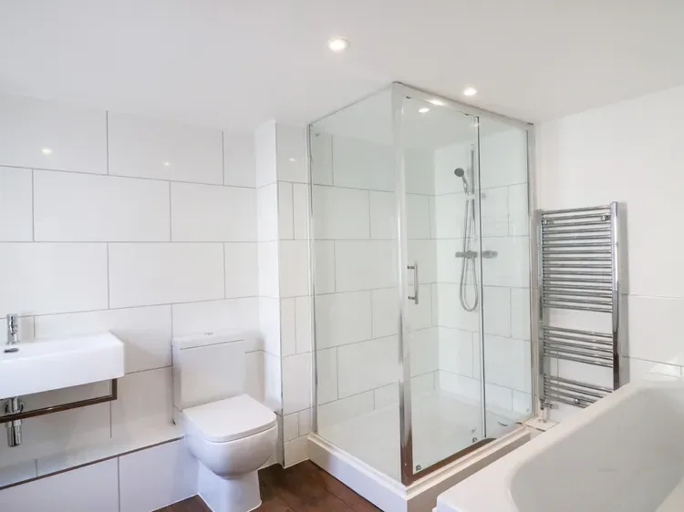 A bright bathroom with a glass shower, sink, toilet, and bathtub.